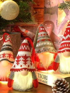 three lighted christmas gnomes sitting on top of a wooden table next to pine cones