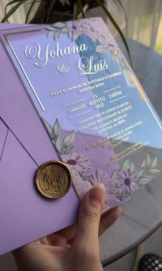 a person holding up a purple and silver wedding card with a wax stamp on it