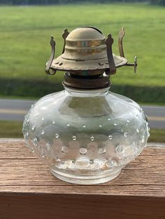 an old fashioned oil lamp sitting on top of a wooden table next to a field