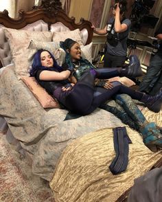 two women laying on top of a bed in a room with other people around them