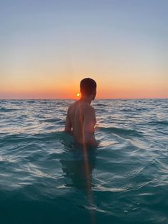 a man sitting in the water at sunset with his back turned to the camera,