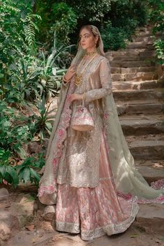 a woman in a white and pink lehenga standing next to some steps with trees