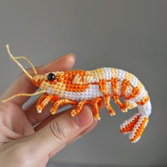 a hand holding an orange and white crocheted gecko