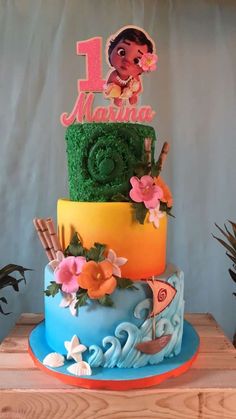 a colorful cake with the number one on top is decorated with grass and flowers, including an image of princess moan