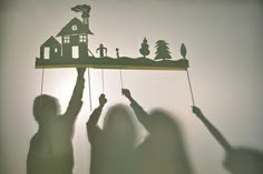 two people holding up a paper cut out of a house and trees on a string