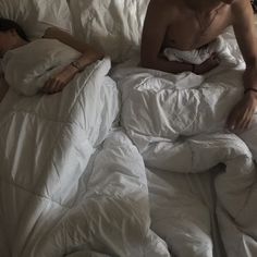 a man laying in bed with an unmade white comforter on top of him