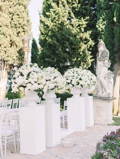 several white vases filled with flowers sitting on top of a stone walkway next to a statue