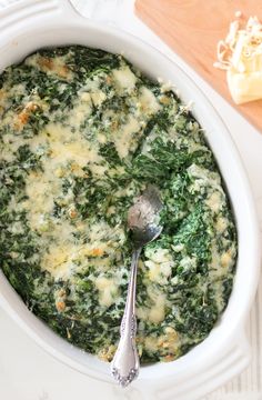 spinach and cheese casserole in a white dish with a spoon on the side