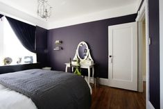 a bedroom with dark purple walls and white furniture, including a large mirror on the wall