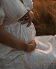 a pregnant woman in white dress sitting on the ground with her belly tucked under her stomach