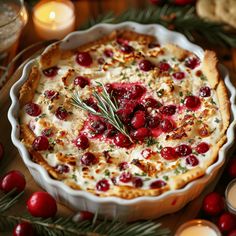 a baked dish with cranberries and herbs in it on a table surrounded by candles