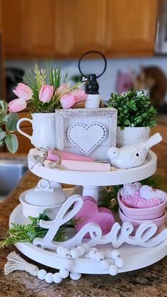 three tiered cake stand with flowers and teacups on it, sitting on a kitchen counter