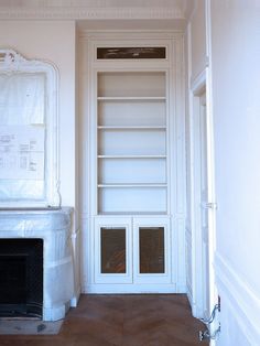 an empty room with a fireplace and white bookcase