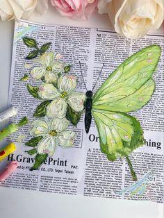 a green butterfly sitting on top of an open book next to flowers and crayons