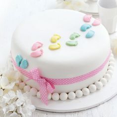 a white cake with pink, yellow and blue decorations on it sitting on a table