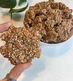 a person holding two cookies in their hand next to a bowl of oatmeal