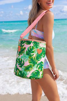 a woman walking on the beach carrying a tropical print tote bag in front of the ocean