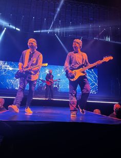 two young men are playing guitars on stage