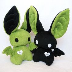 two stuffed animals sitting next to each other on a white surface with one black and one green