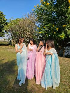 four women dressed in pastel colored saris are standing together and talking to each other