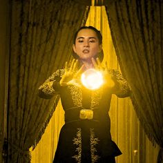 a woman holding a ball in front of her face while standing next to curtained windows