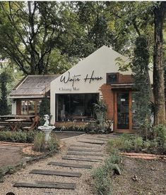 a white building sitting next to a forest filled with lots of green plants and trees