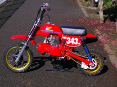 a red and yellow dirt bike parked on the side of a road next to flowers