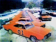 an orange race car is parked in a parking lot with other cars and trucks behind it