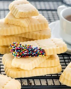 some cookies with sprinkles are on a cooling rack next to a cup of coffee