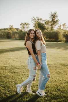 two girls are standing in the grass and hugging each other with their arms around one another