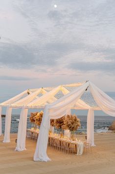 an outdoor wedding setup on the beach with white draping and flowers in vases