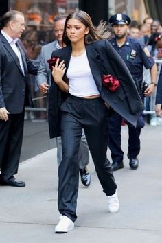 a woman walking down the street in a suit and white top with flowers on her lap