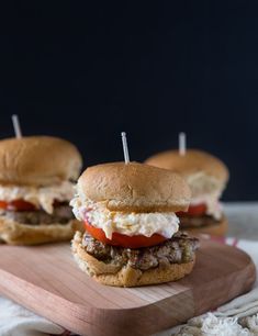 two hamburgers with meat and tomatoes on a cutting board next to some toothpicks