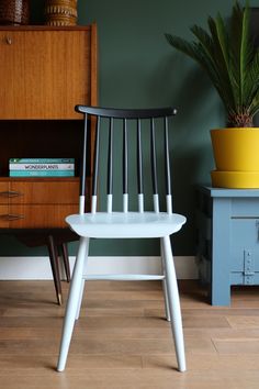 a white chair sitting in front of a wooden dresser next to a potted plant