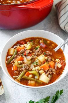 a white bowl filled with soup next to a red casserole dish full of meat and vegetables