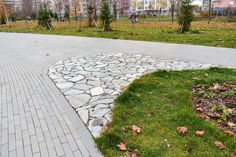 a stone path in the middle of a park with grass and leaves on it, surrounded by buildings