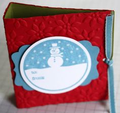 a red and blue card with a snowman sticker on the front, sitting on top of a table