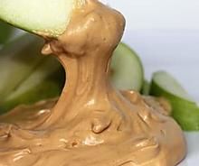 an apple being dipped with peanut butter on a plate