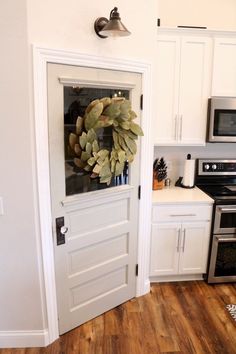 a door with a wreath hanging on it in a kitchen next to an oven and microwave