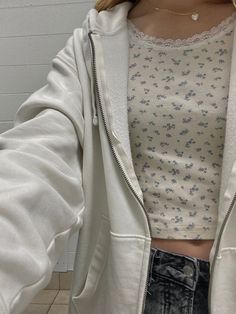 a woman taking a selfie with her cell phone in the bathroom while wearing a white jacket and jeans