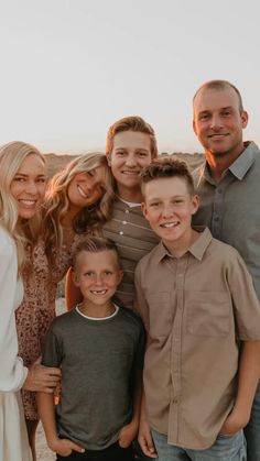 a group of people standing next to each other in front of the ocean at sunset