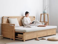 a woman sitting on top of a wooden couch next to a white rug and pillows