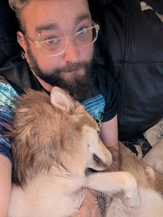 a man laying on top of a couch next to a brown and white husky dog