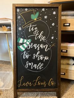 a chalkboard sign that says tis the season to shop smile with a snowman on it