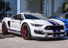 a white ford mustang with blue stripes parked in front of a car dealership window