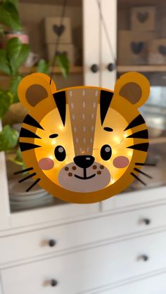 a lighted tiger head hanging from the side of a white cabinet next to a potted plant