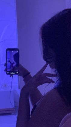 a woman taking a selfie with her cell phone in front of the camera and blue light behind her