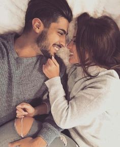 a man and woman laying on top of a bed next to each other smiling at each other