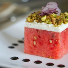 a piece of watermelon with white cream and pistachios on top