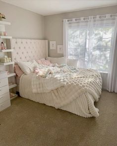 a white bed sitting in a bedroom next to a window with curtains on the windowsill